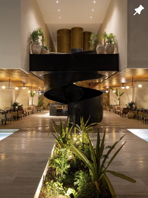 Lobby con escalera escultórica y vegetación