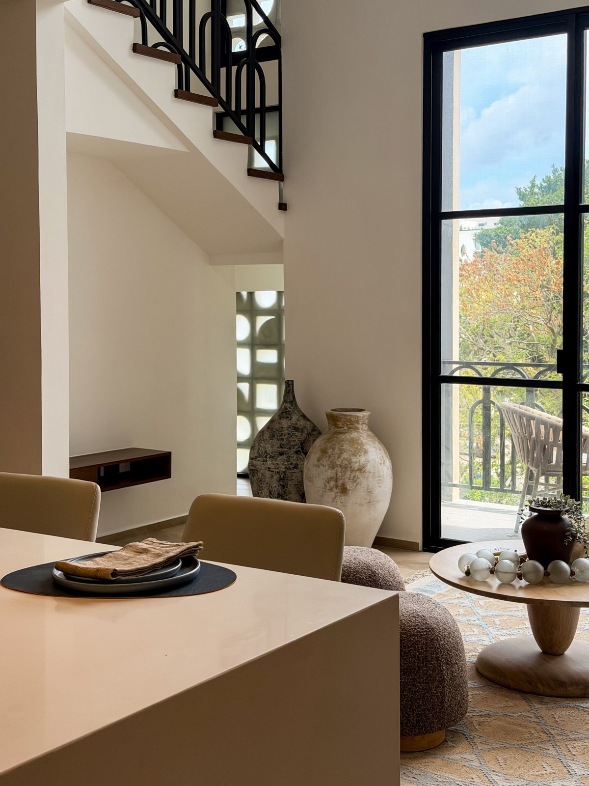 Interior de una residencia con doble altura, escalera de herrería y ventanal hacia la terraza